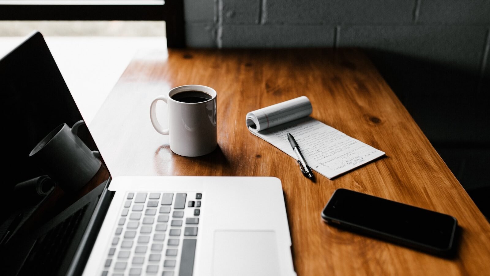 MacBook Pro, white ceramic mug,and black smartphone on table